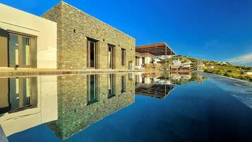 A modern villa with a stone facade, a swimming pool, and a clear reflection.