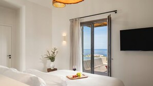 Una camera d'albergo con un letto, una TV a schermo piatto, una finestra vista mare e una lampada a soffitto in legno.