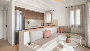 A modern living room with a beige sofa, a white coffee table, and a kitchen area with wooden cabinets and a stainless steel refrigerator. - Villa Gaione, Divine Sea Views, Private Infinity Pool, Furnished Terrace, Sifnos (Sifnos)
