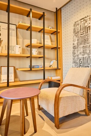 A cozy seating area with a cushioned chair and a small round table, wooden shelves with various items, and a decorative wall with geometric patterns. - Terrasses & Sunset • Duplex Luxe 3 Bed in Ghandi (Casablanca)