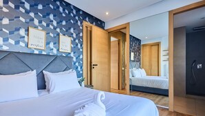 Ein modernes Hotelzimmer mit einem großen Bett, einer Kopfteil und einer Wand mit geometrischen Mustern. An der Wand befinden sich zwei gerahmte inspirierende Zitate.