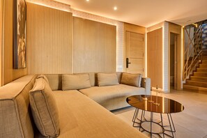 A modern living room with a beige sectional sofa, a round coffee table, and a staircase leading to another level. - Terrasses & Sunset • Duplex Luxe 3 Bed in Ghandi (Casablanca)