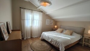 Une chambre à coucher avec un lit, une table de chevet avec une lampe, une fenêtre avec des rideaux et un luminaire au plafond.