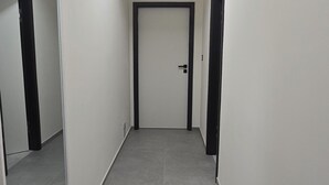 Un couloir étroit, avec une porte au fond, un banc sur le côté gauche et un miroir sur le mur gauche.