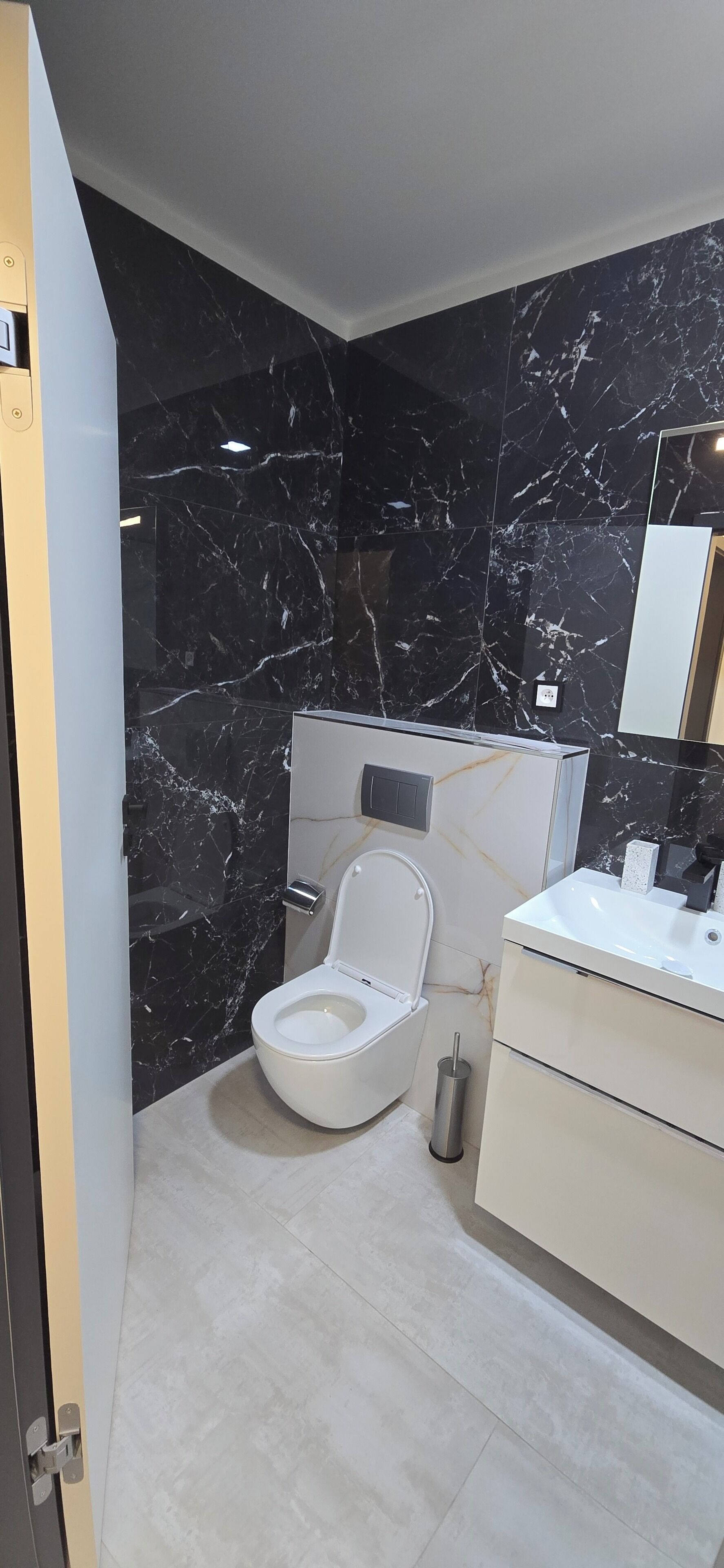Un baño moderno con inodoro y lavamanos blancos, y un espejo sobre el lavamanos.