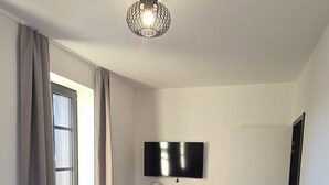 Une chambre à coucher avec un lit, une commode, un téléviseur et une fenêtre avec des rideaux.