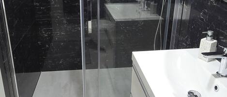 Un baño moderno con ducha envuelta en vidrio, un lavabo blanco y un salpicadero de mármol.