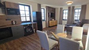 Cuisine moderne équipée d’un four à micro-ondes, d’un réfrigérateur et d’un lave-linge. Un coin salon avec des chaises et une table est également à disposition.