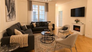 Een woonkamer met een bank, fauteuils, een salontafel, een open haard en een televisie.