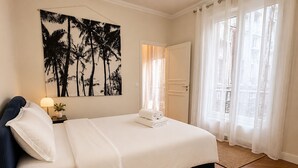 Een hotelkamer met een bed, een nachtkastje, een aan de muur hangend schilderij, een deur en een raam met gordijnen.