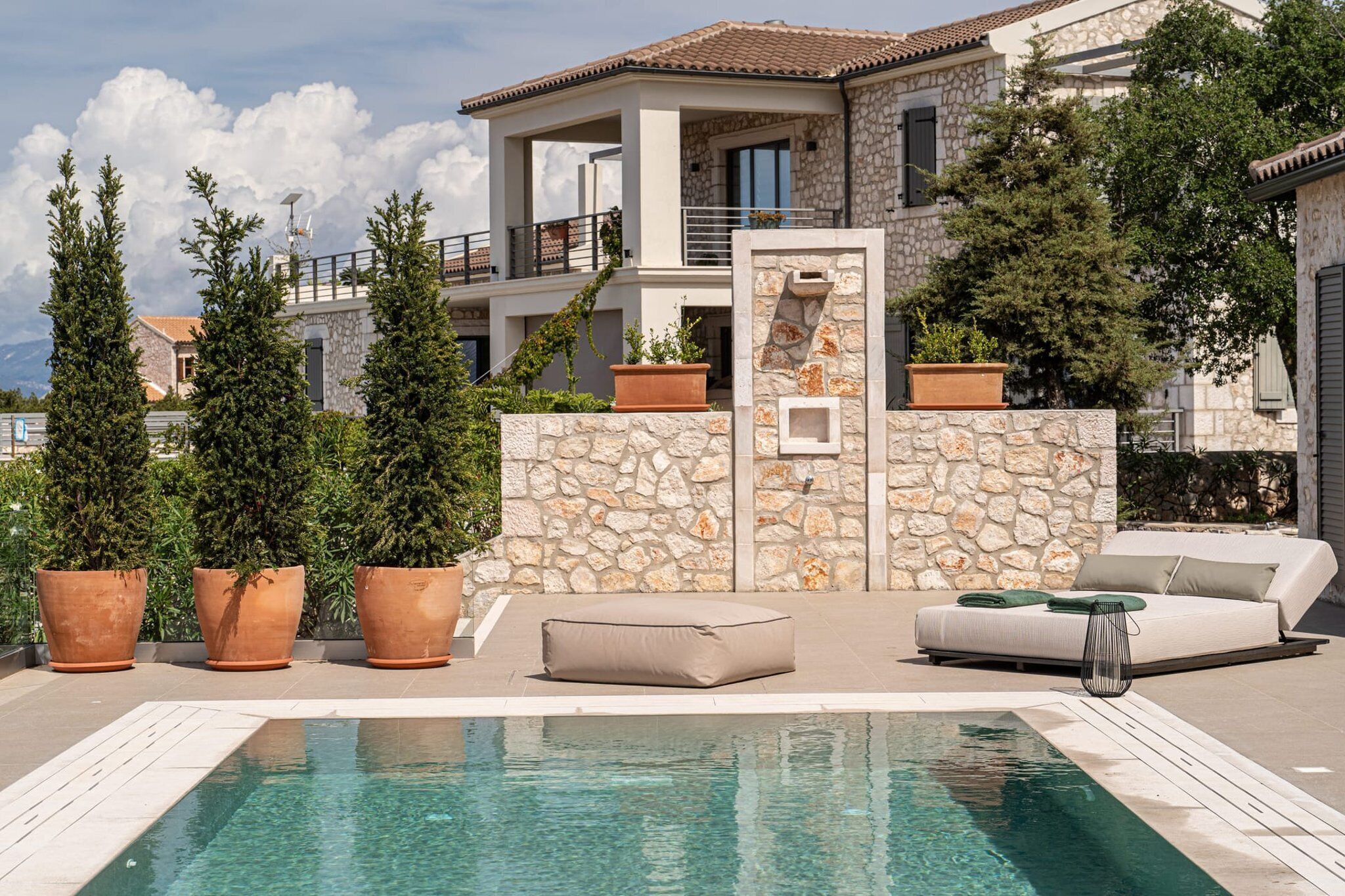 A modern villa with a stone facade, a swimming pool, and outdoor seating.