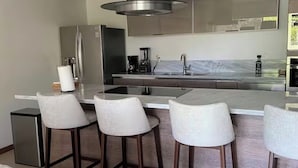 A modern kitchen with a stainless steel range hood, a marble countertop, and four bar stools. - PENINSULA NUEVO VALLARTA BEAUTIFUL CONDOMINIUM (Las Jarretaderas)