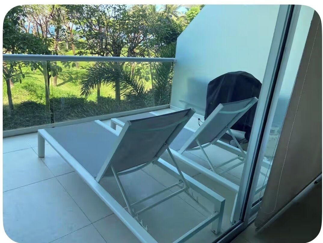 A balcony with a glass table and chairs, overlooking a garden.