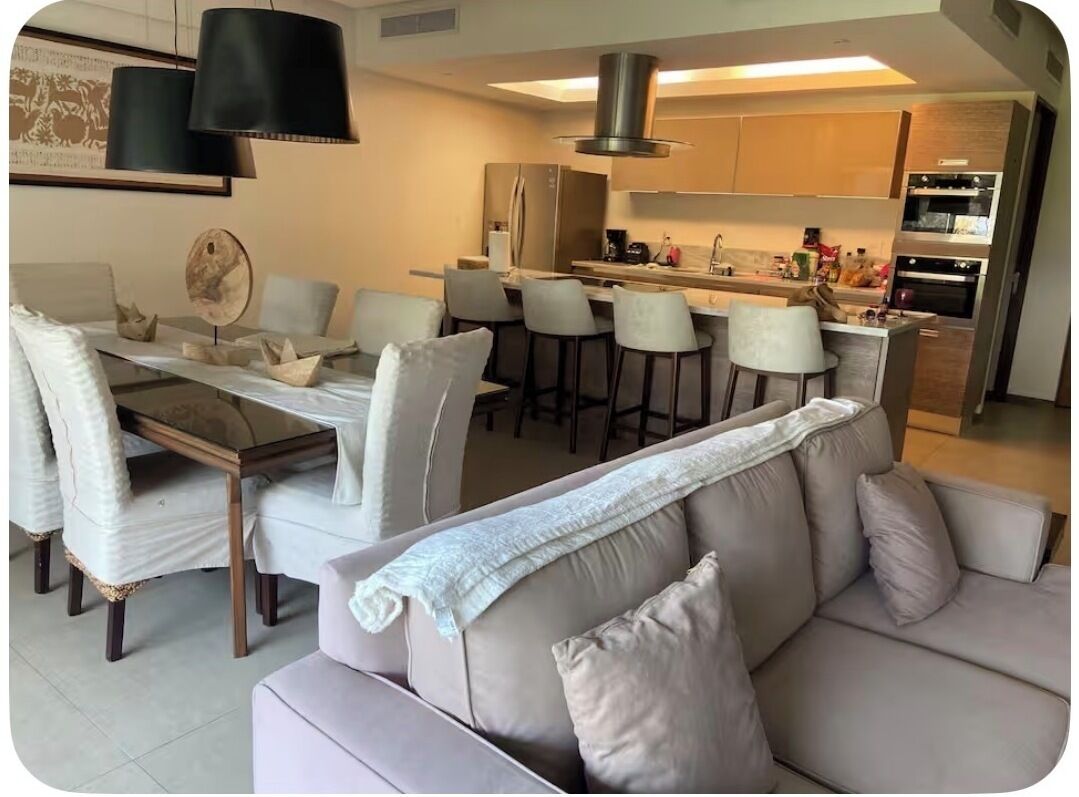 A modern kitchen with a central island, bar stools, and a dining table with chairs.