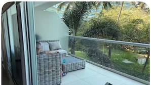 A balcony with wicker furniture, a glass railing, and a view of greenery. - PENINSULA NUEVO VALLARTA BEAUTIFUL CONDOMINIUM (Las Jarretaderas)