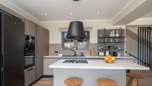 A modern kitchen with a central island, wooden stools, a black pendant light, and a view of the outdoors through a window. - Villa Philaea, Divine Sea Views, Private Pool, Furnished Terrace, Kefalonia (Kefalonia)