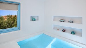 Casa de banho moderna com banheira integrada, janela com vista para vegetação e objetos decorativos nas prateleiras.
