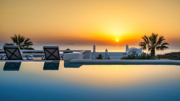 Piscina infinita com espreguiçadeiras e vista do pôr do sol sobre o mar.