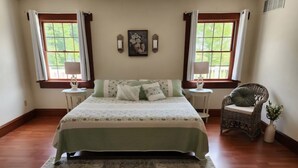 Een slaapkamer met een groot bed, twee nachtkastjes, een stoel en een raam met gordijnen.