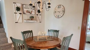 Een eetgedeelte met een ronde houten tafel, vier stoelen, een klok en decoratieve wandobjecten.