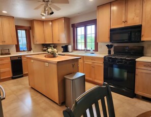 A kitchen with wooden cabinets, a central island, a black stove, and a ceiling fan. - Peaceful Country Manor Close to Kenyon and Mt. Vernon (Gambier)