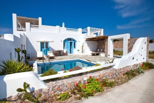 Una villa blanca con piscina, muros de piedra y una puerta azul.