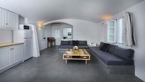 Een moderne woonruimte met een keuken, een grijze bank, een houten salontafel en een groot raam met gordijnen.