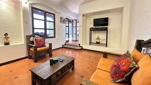 Una sala de estar con un sofá, una mesa de centro de madera, una silla con cojín, una chimenea y un televisor montado en la pared.