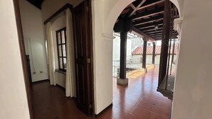 Un pasillo con suelo de baldosas, una puerta de madera y vista a un área de balcón exterior con suelo de cerámica y barandilla.