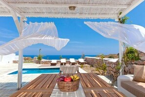A covered outdoor seating area with a pool and lounge chairs, overlooking a clear blue sky and ocean. - Villa Solaryth, Divine Sea Views, Private Pool, Furnished Terrace, Santorini (Santorini)
