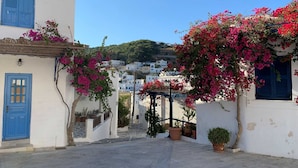 A narrow street with white buildings, blue doors, and pink bougainvillea flowers. - Villa Helionis, Divine Sea Views, Private Plunge Pool, Furnished Terrace,. (Santorini)