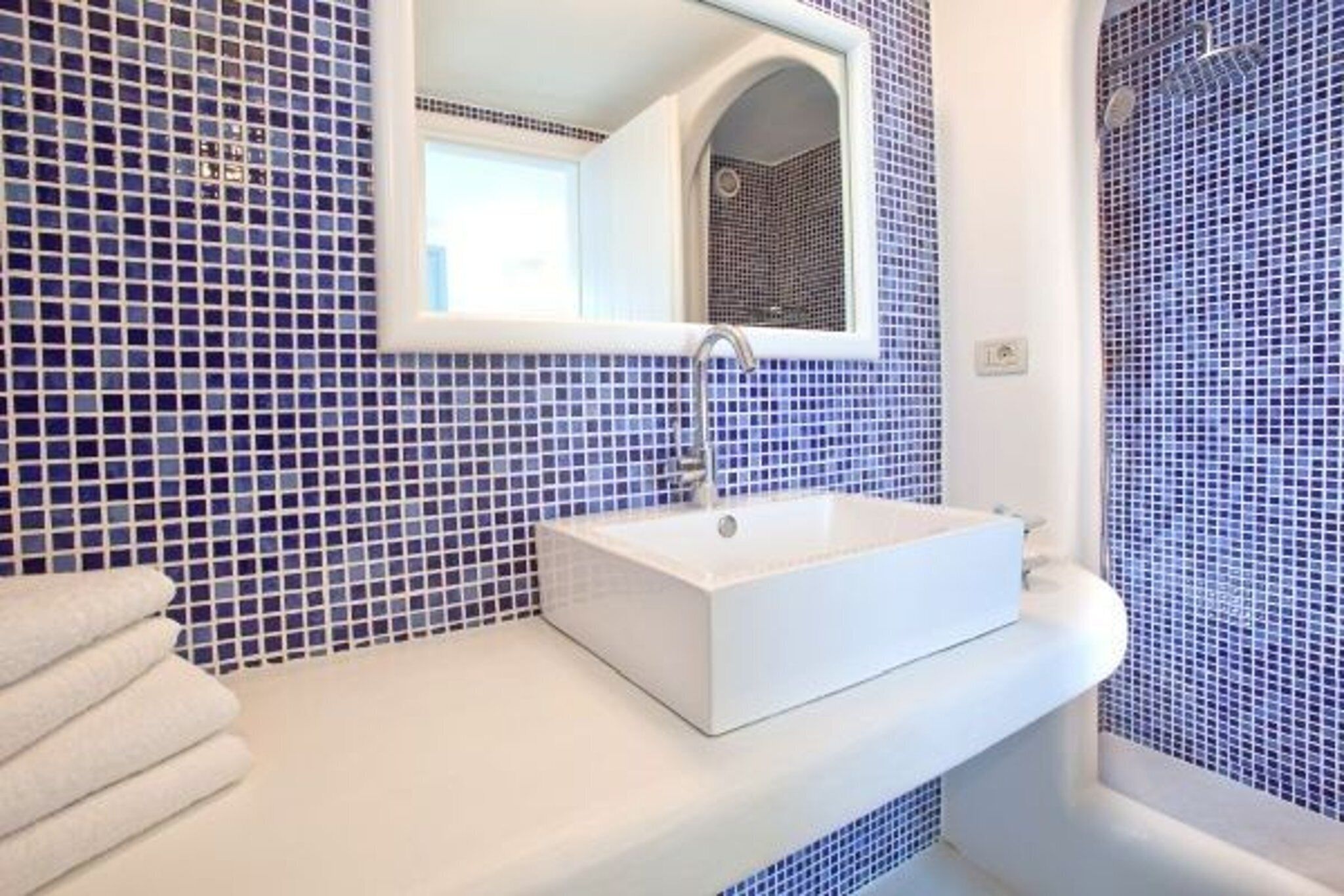 A bathroom with a white sink, a mirror, and blue mosaic tiles.