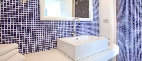 A bathroom with a white sink, a mirror, and blue mosaic tiles.