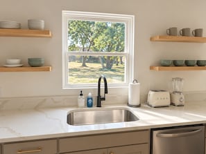 A kitchen with a window, stainless steel sink, wooden shelves, and modern appliances. - The Loves’ Shack With Fire Pit, EV Charger, near I40, AR Nuclear 1 & Data Center (Clarksville)