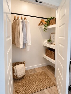 A walk-in closet with hanging clothes, shelves with baskets, a framed sign, and a woven rug. - The Loves’ Shack With Fire Pit, EV Charger, near I40, AR Nuclear 1 & Data Center (Clarksville)