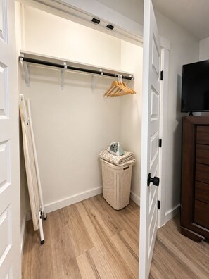 A walk-in closet with a wooden floor, a hanging rod, a basket, and a television on a cabinet. - The Loves’ Shack With Fire Pit, EV Charger, near I40, AR Nuclear 1 & Data Center (Clarksville)