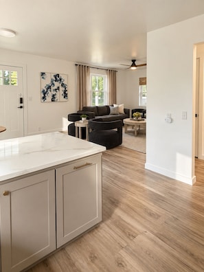 A modern kitchen with a marble countertop and wooden cabinets, a dining area with a table and chairs, and a living room with a sofa and a coffee table. - The Loves’ Shack With Fire Pit, EV Charger, near I40, AR Nuclear 1 & Data Center (Clarksville)