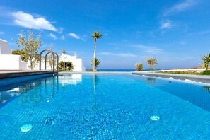 Ein klares, blaues Schwimmbecken mit Blick auf das Meer, umgeben von weißen Gebäuden und Palmen.