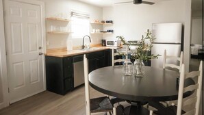 Una cucina moderna con un tavolo da pranzo rotondo, sedie bianche, un frigorifero, un forno a microonde e una ventola a soffitto.