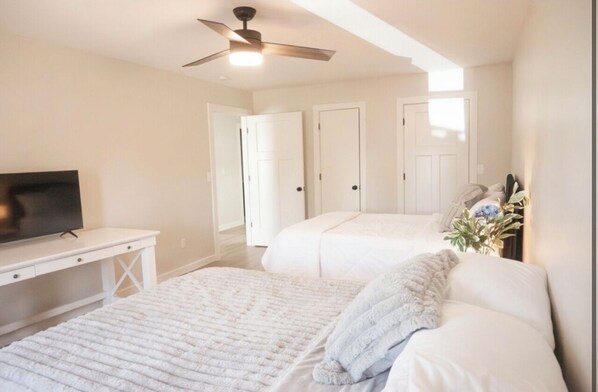 A bedroom with two beds, a TV, and a ceiling fan.