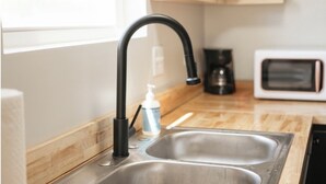 Una cucina con lavello in acciaio inossidabile, un rubinetto nero, un forno a microonde bianco e un piano di lavoro in legno.