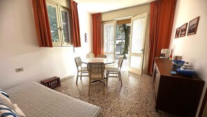 Una stanza compatta con un letto, un tavolo da pranzo con sedie, un angolo cottura e vista attraverso una porta.