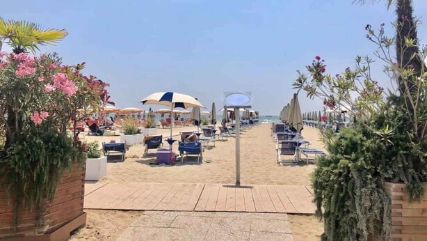 Una passeggiata sulla spiaggia che conduce a una fila di sedie a sdraio e ombrelloni.