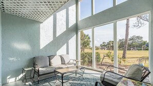 Una habitació il·luminada pel sol amb un sofà, una taula de centre i vista a una zona verda amb arbres.