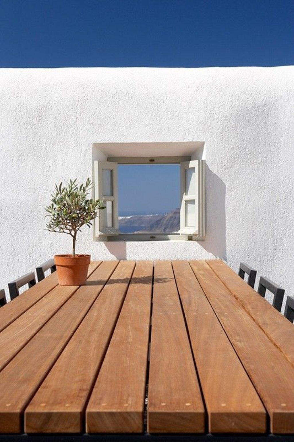 Une table en bois, ornée d’un pot de fleurs, et une fenêtre donnant sur un paysage pittoresque.