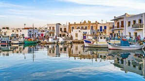 A harbor with boats docked, buildings with balconies, and a calm water surface reflecting the structures. - Villa Noctessa, Divine Sea Views, Private Hot Tub, Furnished Terrace, Pyrgos (Santorini)