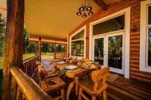 A wooden deck with a dining table set for a meal, surrounded by wooden chairs. - Bunkhouse — Ranch Estate, Private Pond, Story WY (Banner)