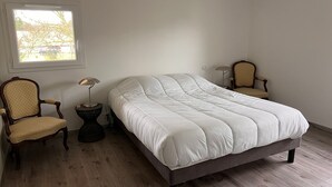 Ett sovrum med en stor säng, två stolar, en lampa och ett fönster.