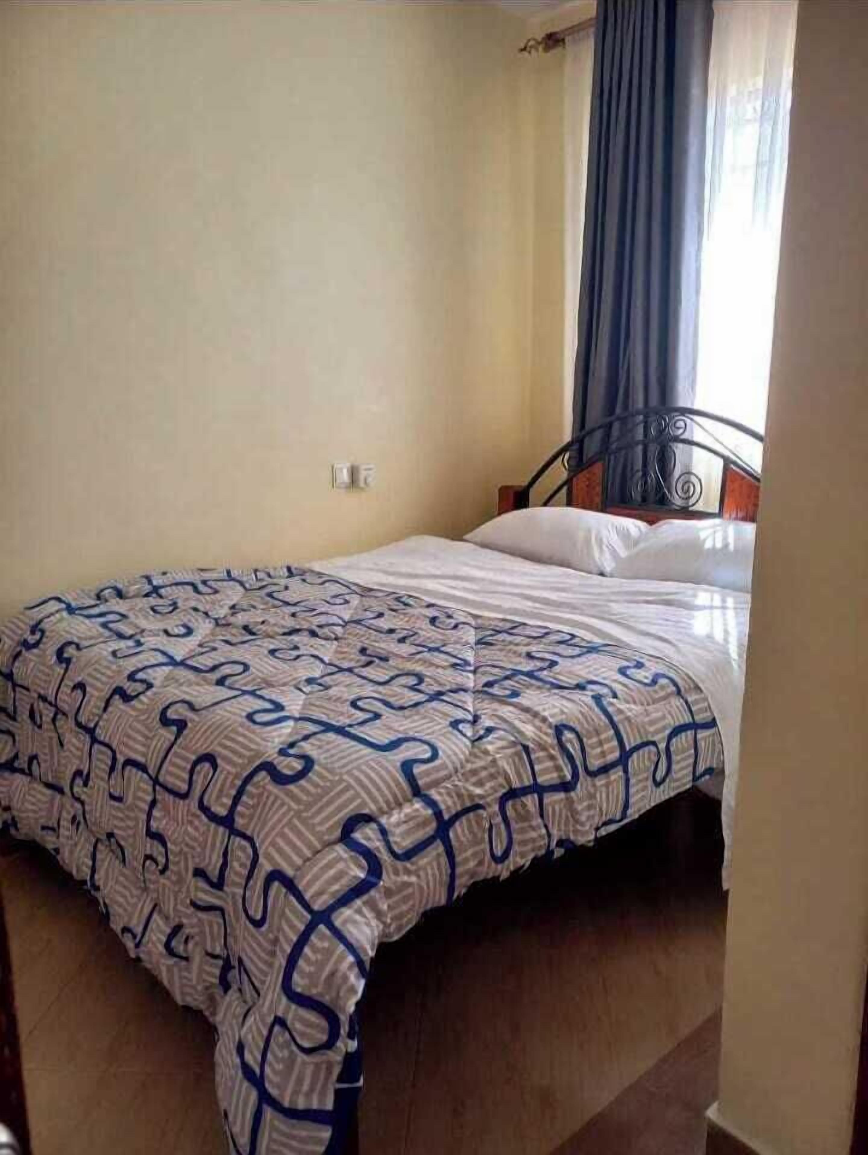 Un llit individual amb un estovat estampat, un capçal de metall i una finestra amb cortines.