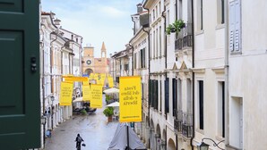 A narrow street with buildings on either side, a cyclist, and yellow banners. - Pordenone historic center (Pordenone)